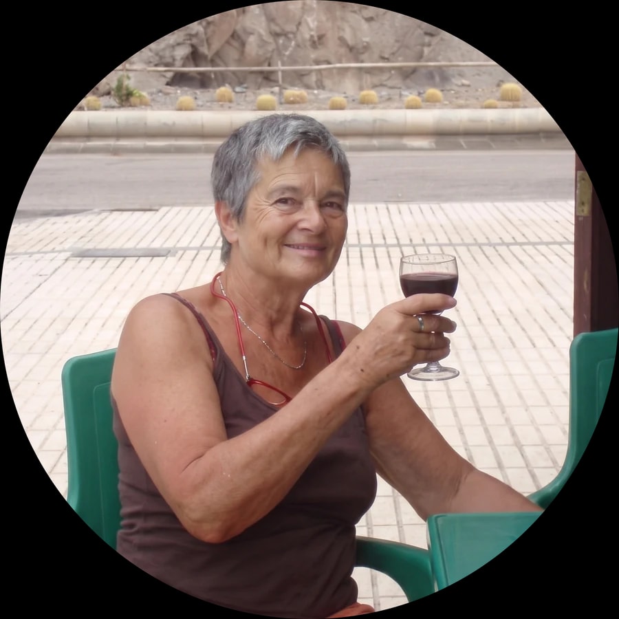 Jacqueline en terrasse, souriante, un verre de vin à la main.